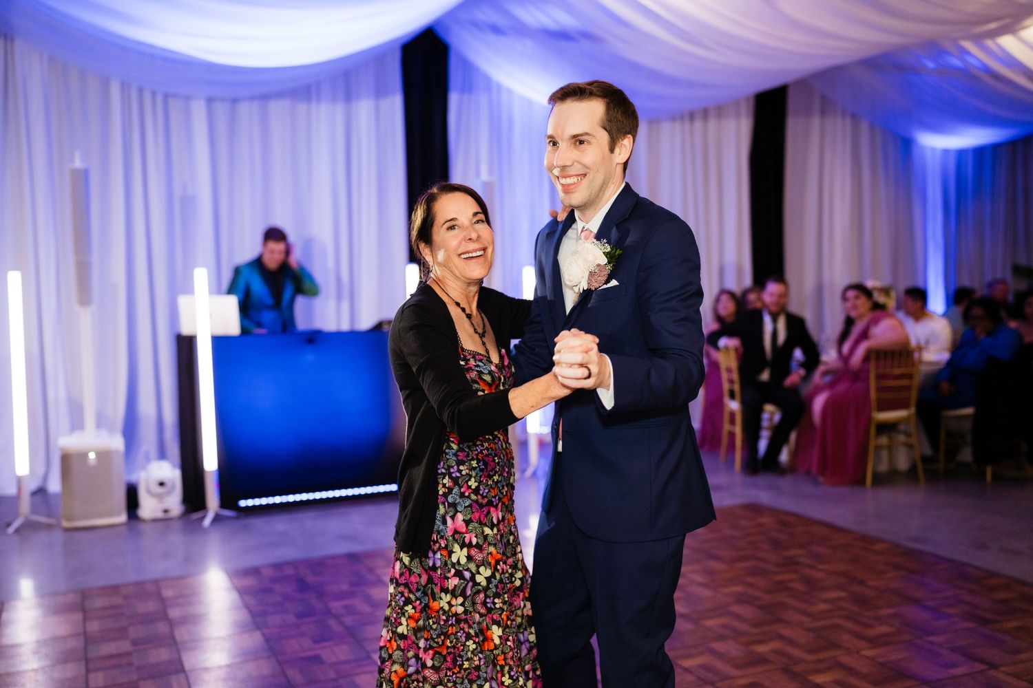 Couple dancing together at an elegant wedding reception with blue uplighting and draped fabric decor.