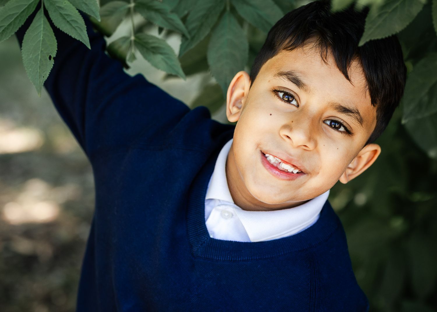A primary aged boy looks relaxed as he swings from a tree and smiles at his Bristol school photoshoot with Little Bodhi Photography.