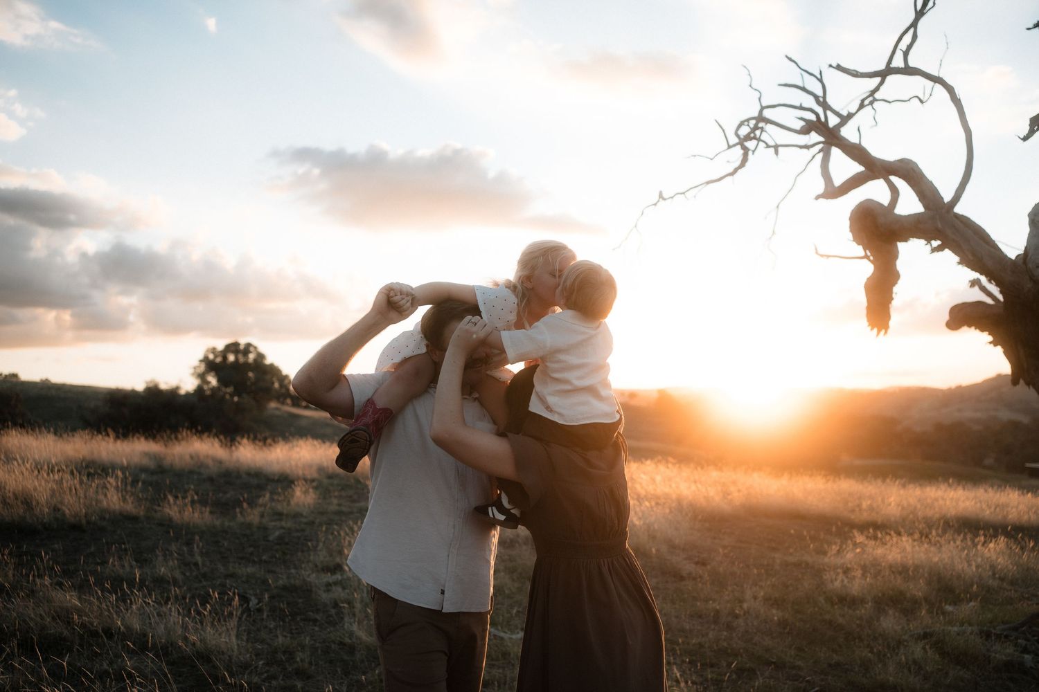 A couple embraces in a golden field during sunset while their photographer captures romantic portraits.