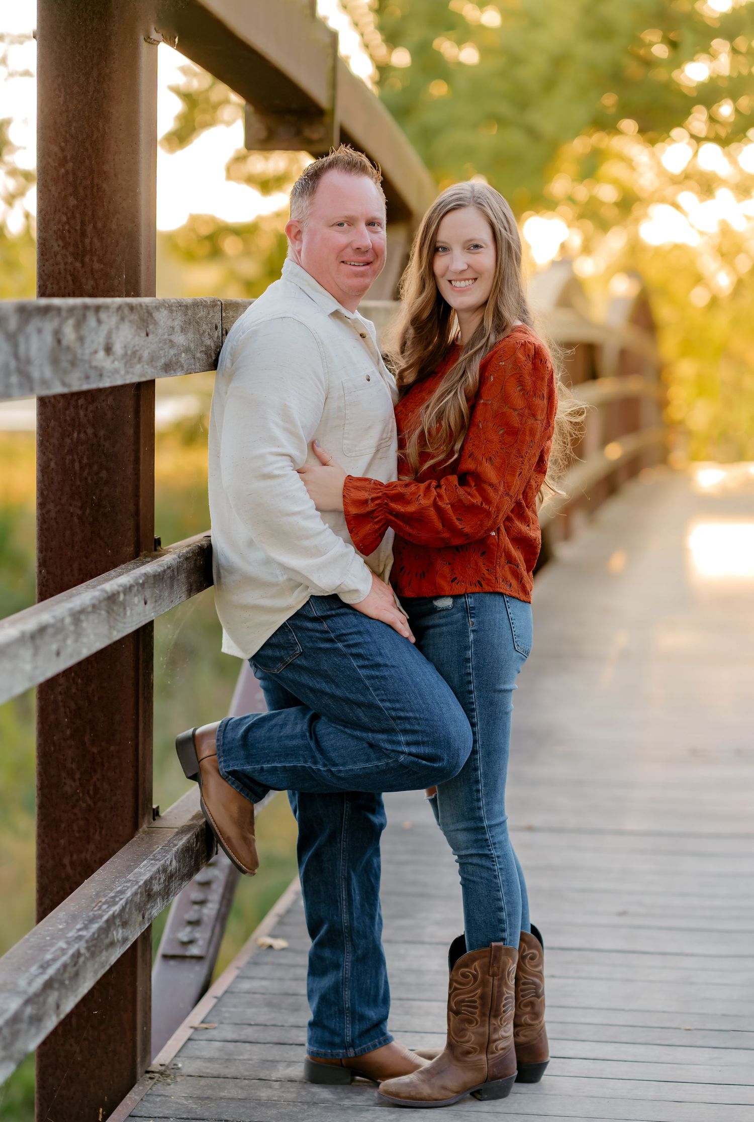 Couple in western attire share romantic moments on a wooden bridge at sunset.