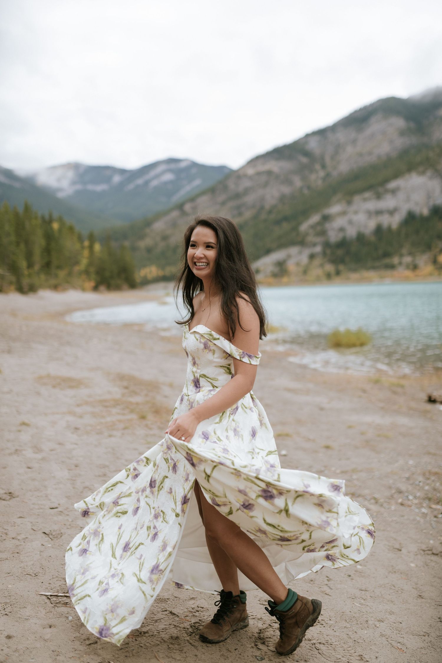A floral dress flows in the mountain breeze as someone twirls by a scenic lake with rugged peaks in the background.