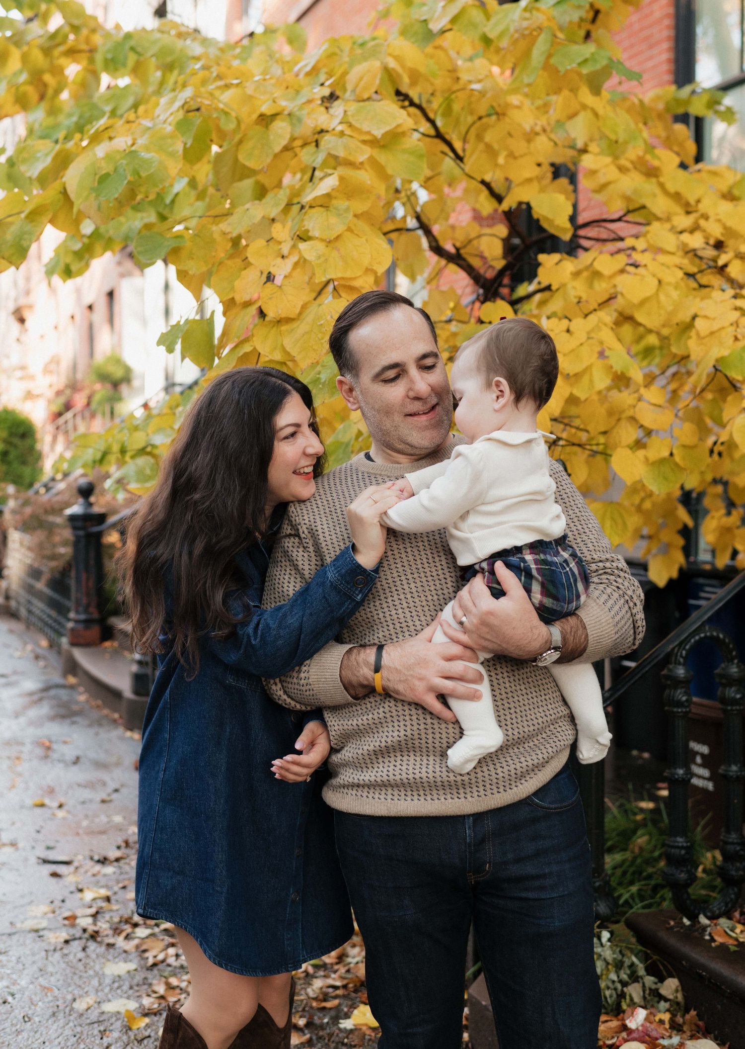 Family enjoying autumn day under golden yellow leaves in casual outdoor photoshoot.