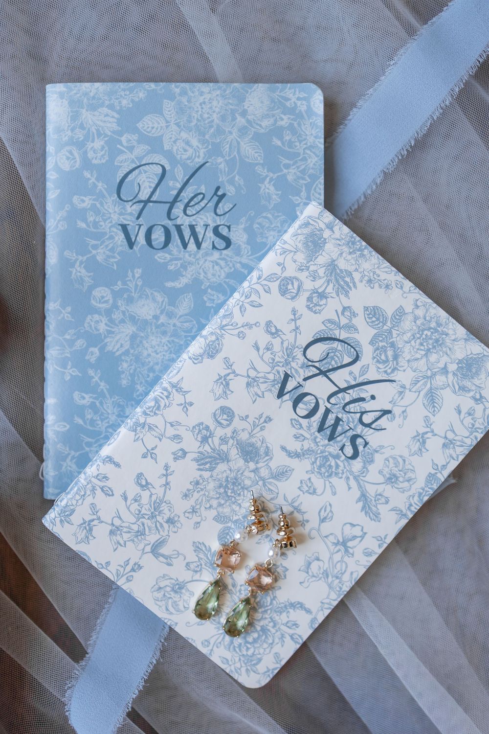 Wedding vow cards and pearl earrings arranged in a delicate blue and white floral pattern display. DALLAS WEDDING PHOTOGRAPHER
