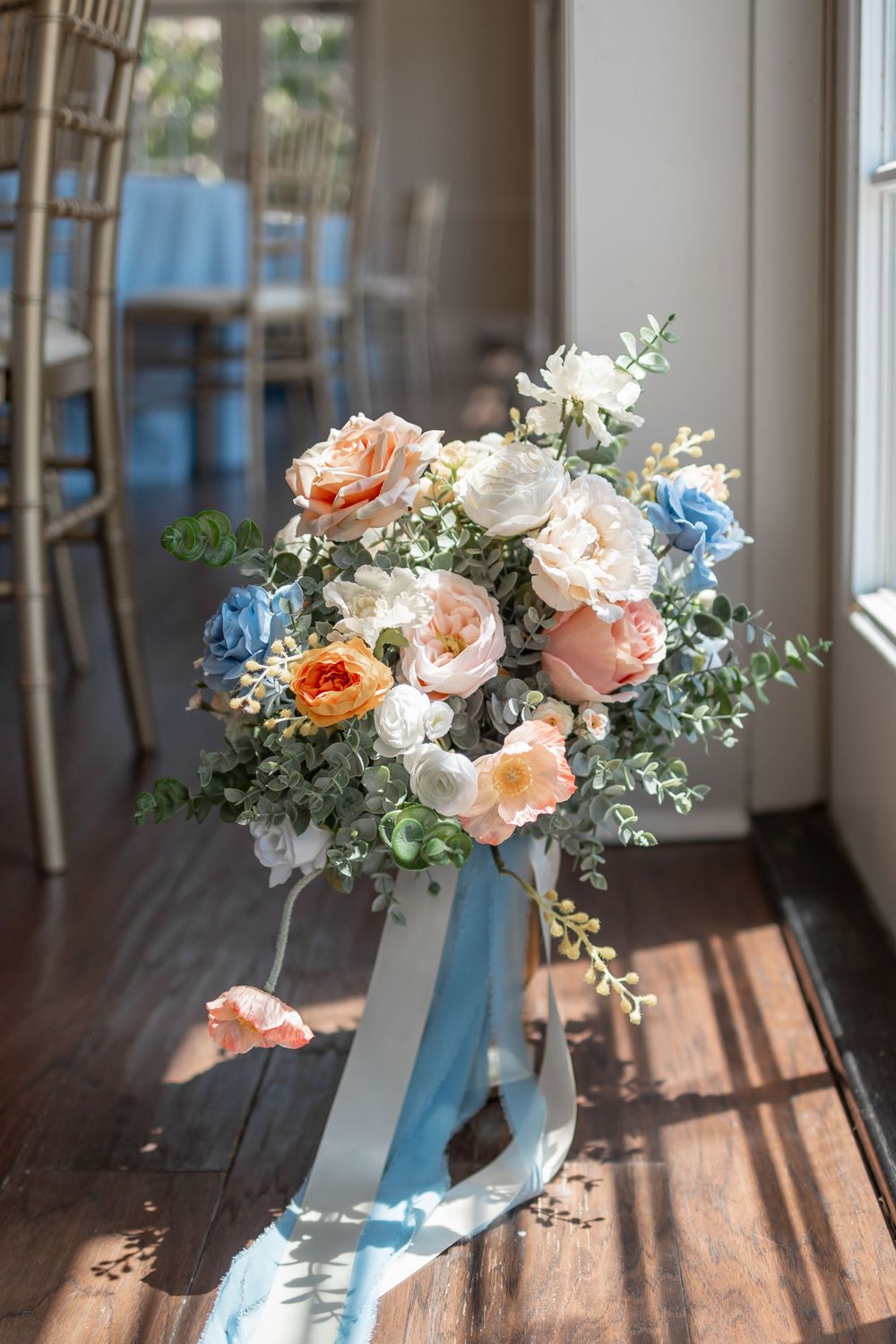 Elegant floral centerpiece with peach roses and blue ribbons on wooden table in natural light. DALLAS WEDDING PHOTOGRAPHER