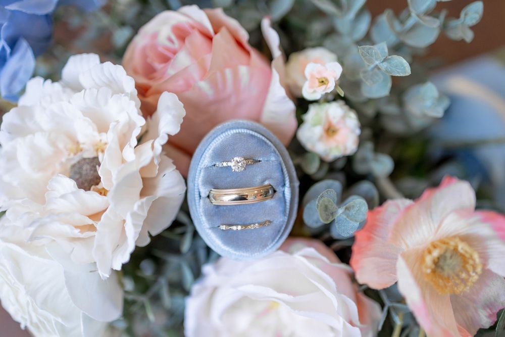 Wedding rings rest delicately on pink and white flowers with eucalyptus leaves in a romantic bridal arrangement. DALLAS WEDDING PHOTOGRAPHER