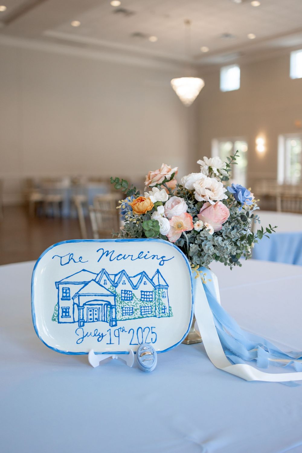 Hand-painted blue and white wedding venue illustration with floral accents decorates a table centerpiece. DALLAS WEDDING PHOTOGRAPHER