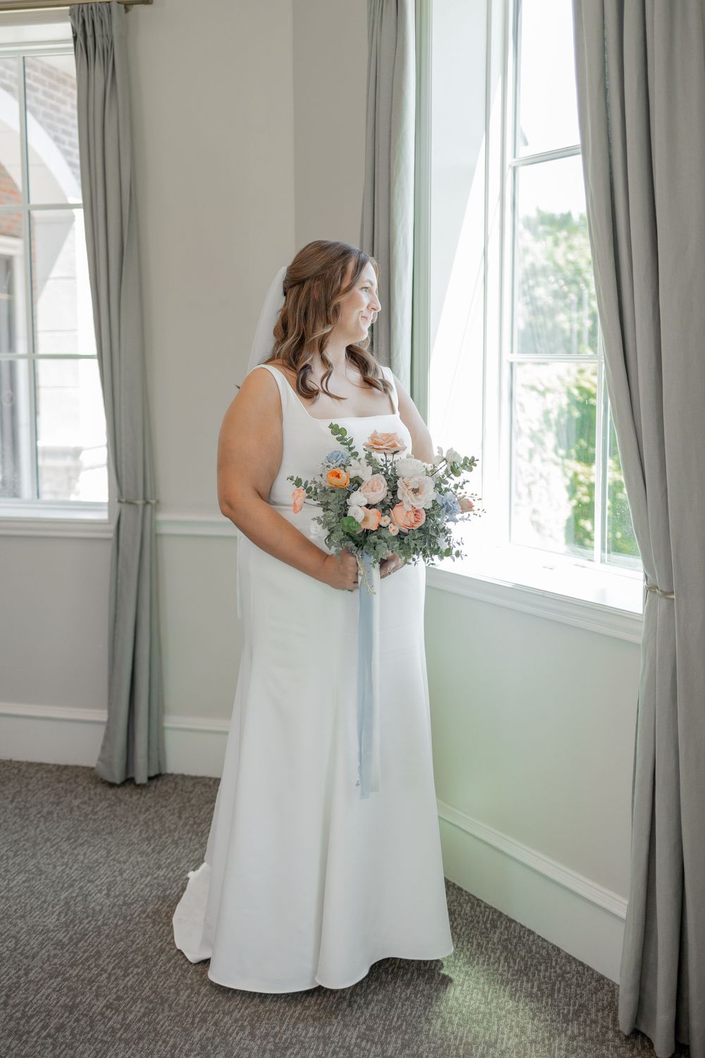 A wedding dress being displayed in an elegant room with natural lighting and gray curtains. DALLAS WEDDING PHOTOGRAPHER