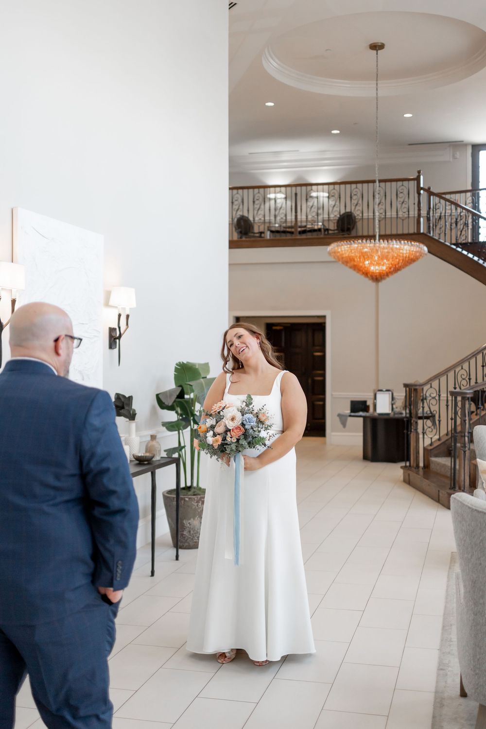 Indoor wedding venue with elegant chandelier and staircase during a first look moment. DALLAS WEDDING PHOTOGRAPHER