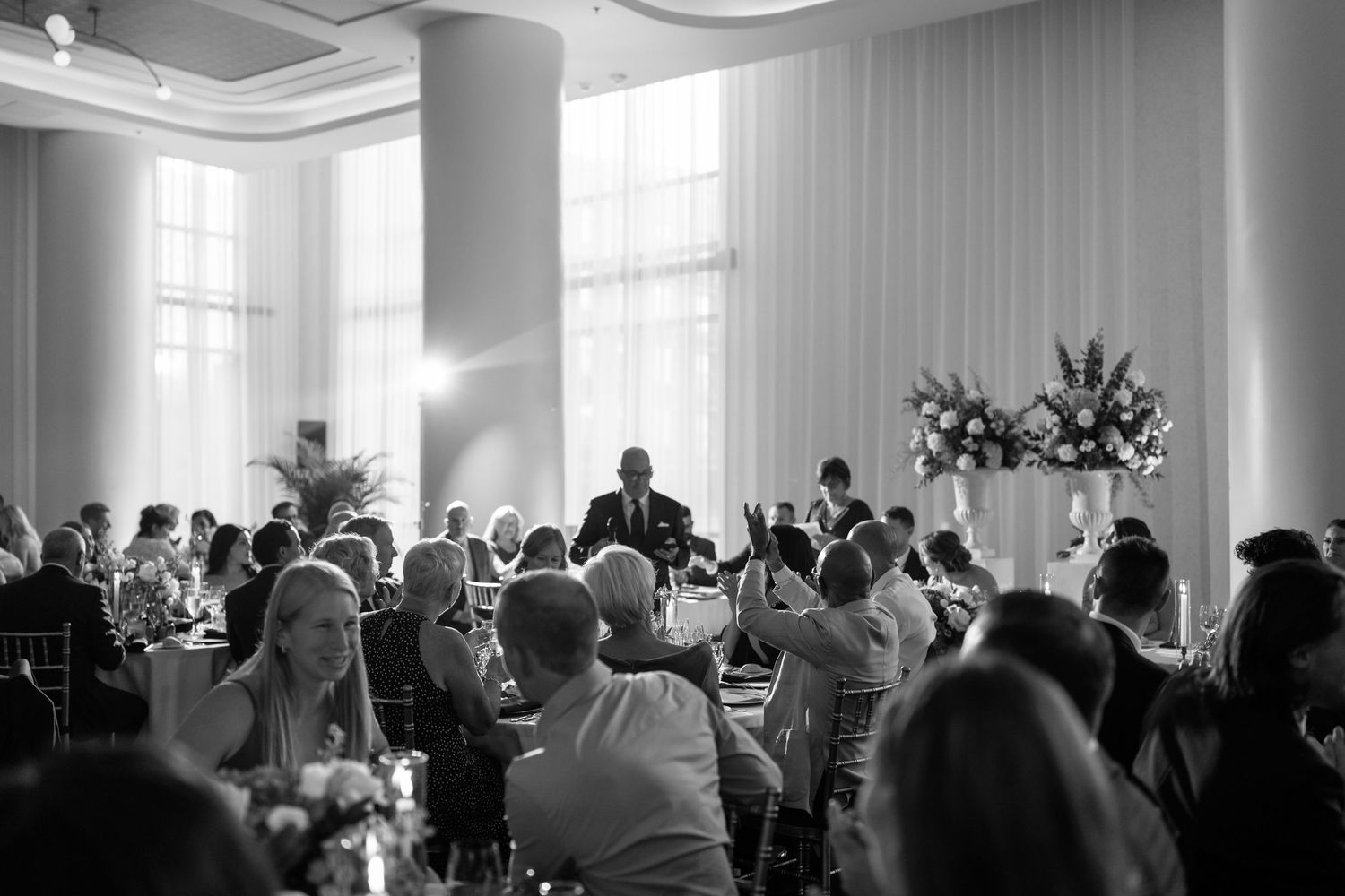 Black and white photo showing guests seated in an elegant ballroom during a wedding ceremony.