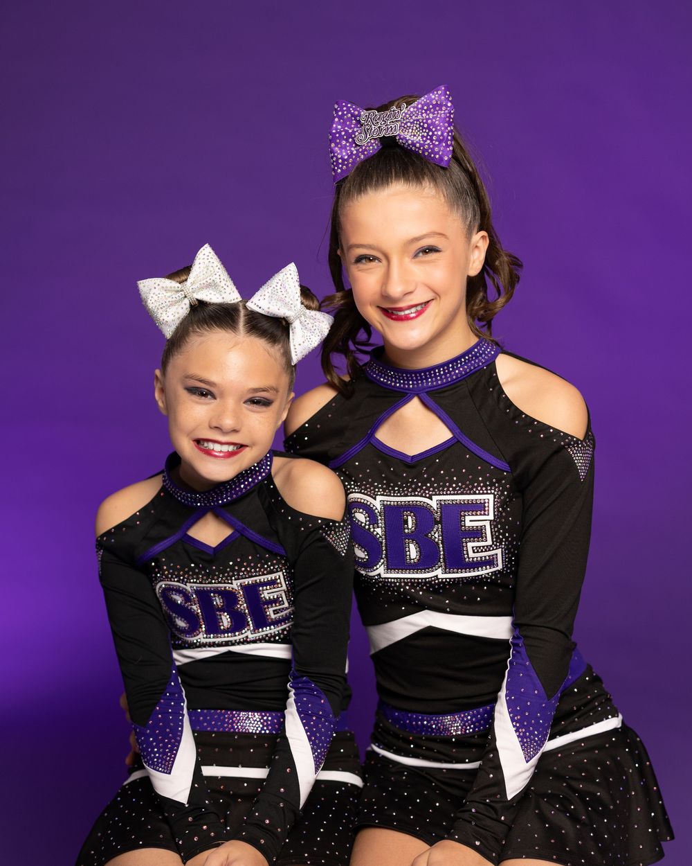 Cheerleaders in purple and black uniforms pose together with matching bows.