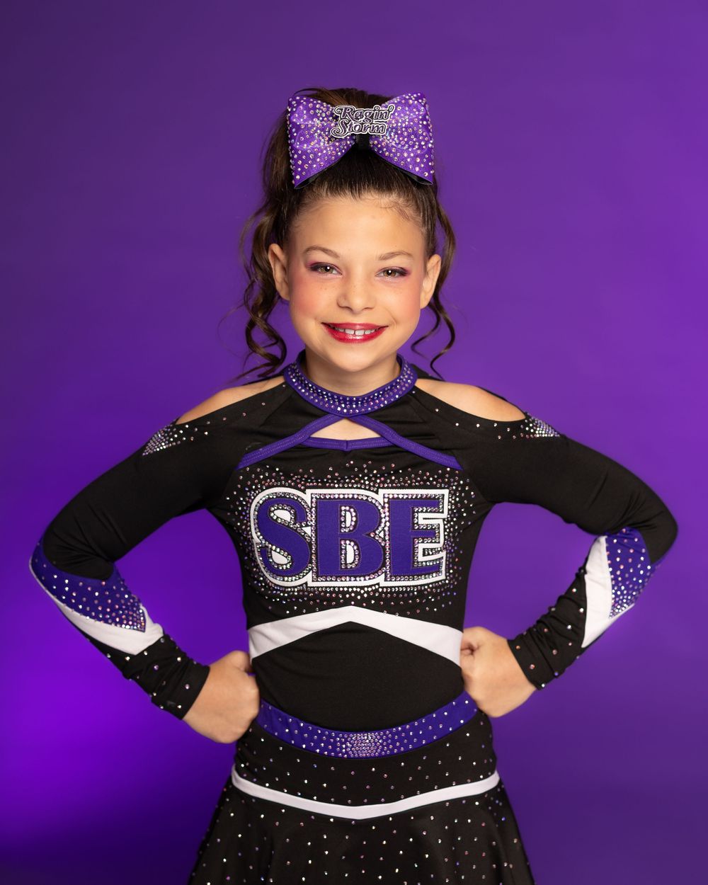 Cheerleader wearing black and purple uniform with SBE lettering strikes confident pose.