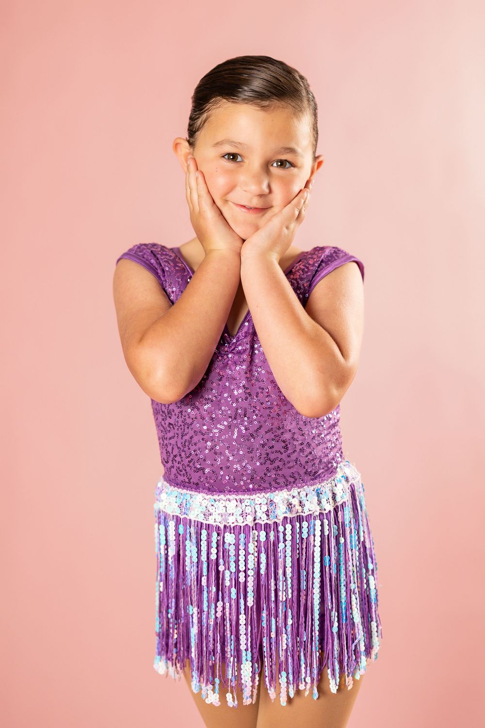 Playful dance portrait with sparkly purple costume and fringe details on pink background.