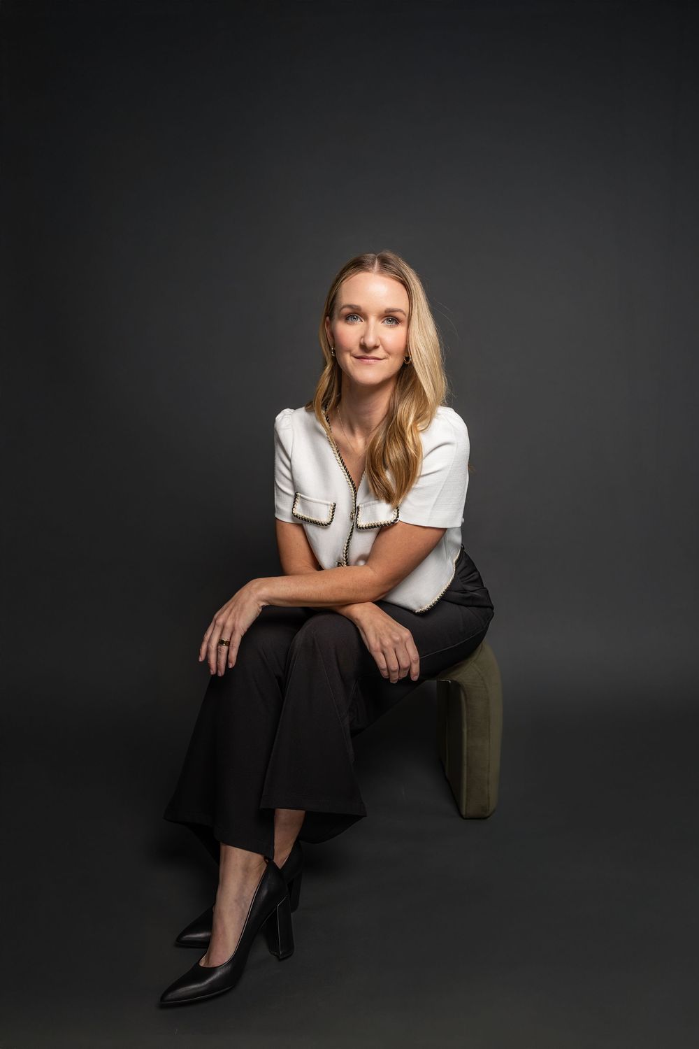 Artistic studio photo with subject seated on olive green furniture against dark backdrop.