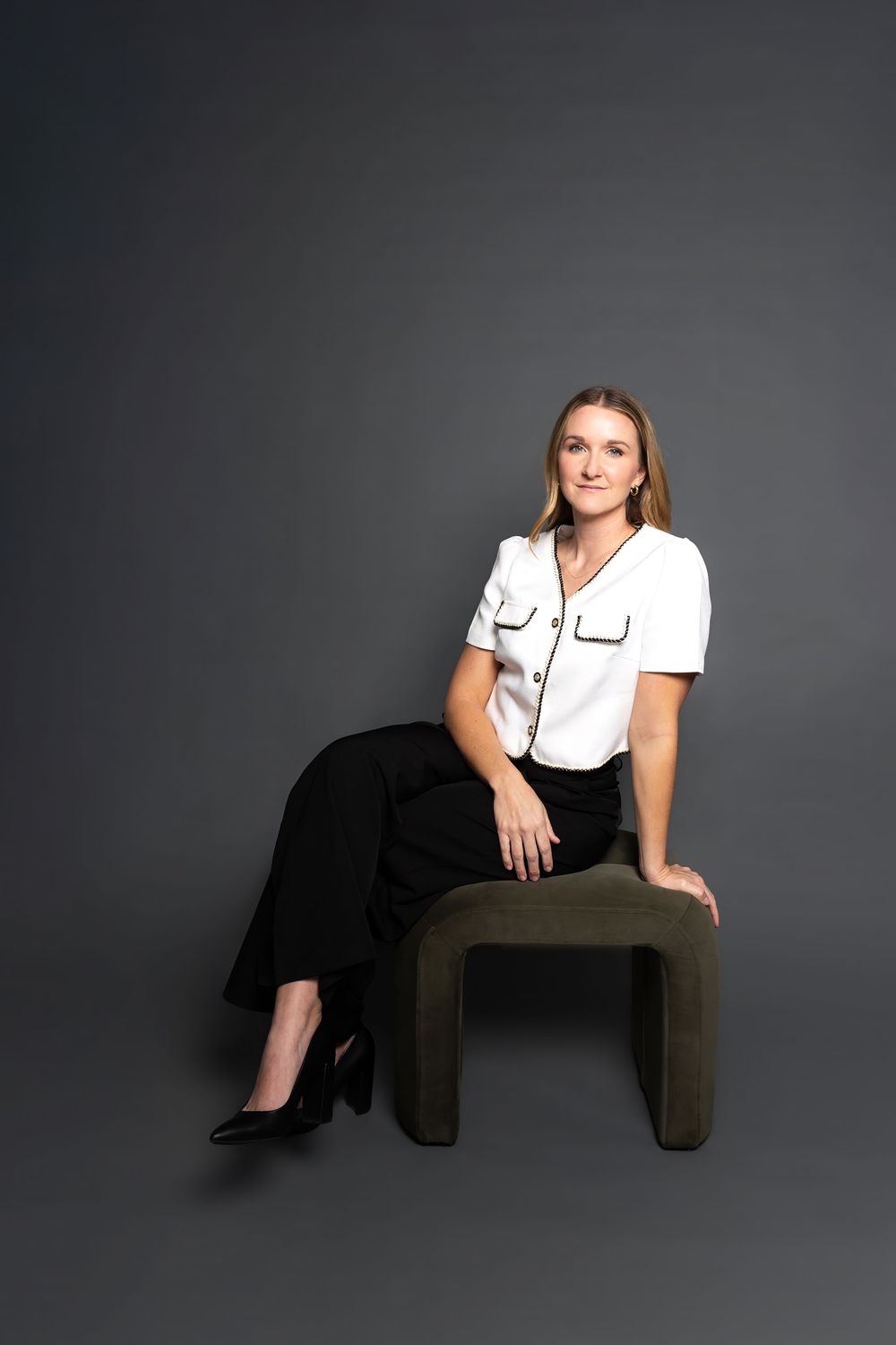 Professional portrait of woman in white shirt and black pants sitting on olive green chair.