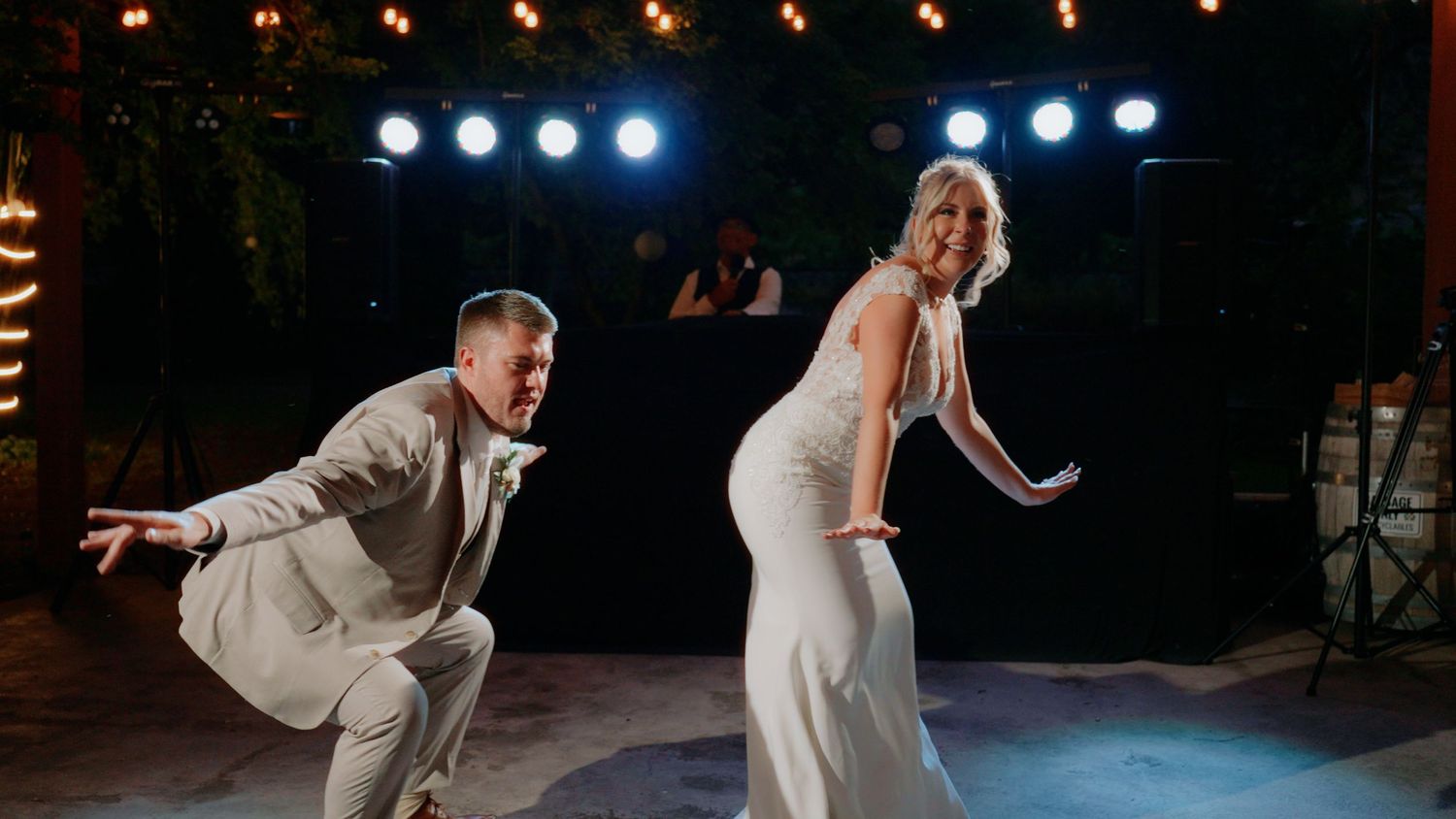A couple performs an energetic first dance at their wedding reception under stage lights.