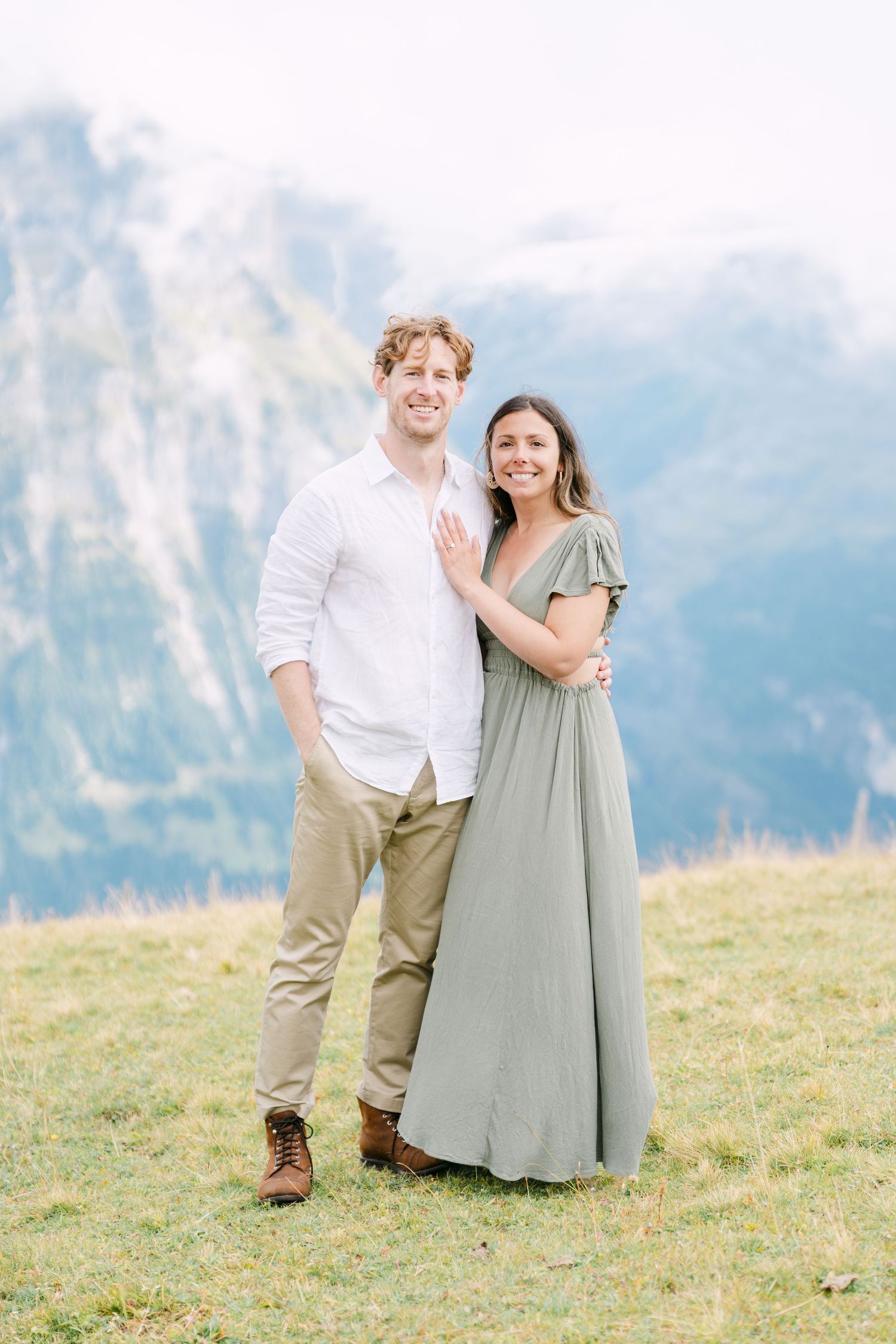 A couple embraces on a grassy hillside with majestic mountain peaks in the background in Grindelwald.