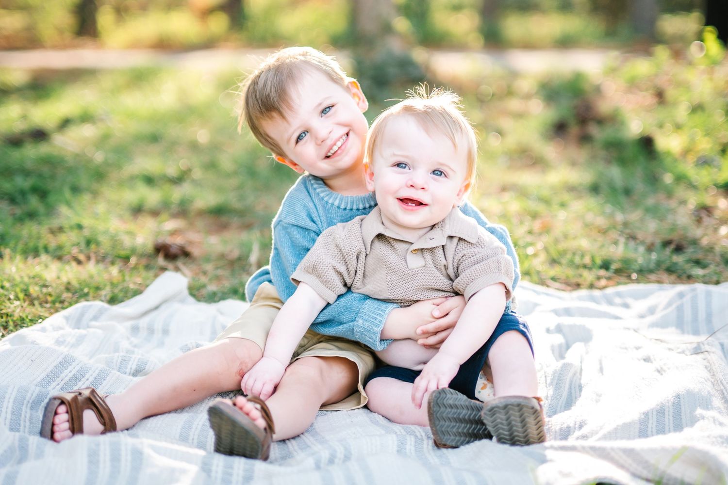 Two happy young brothers sitting together on a blanket during an outdoor fall family photo session.