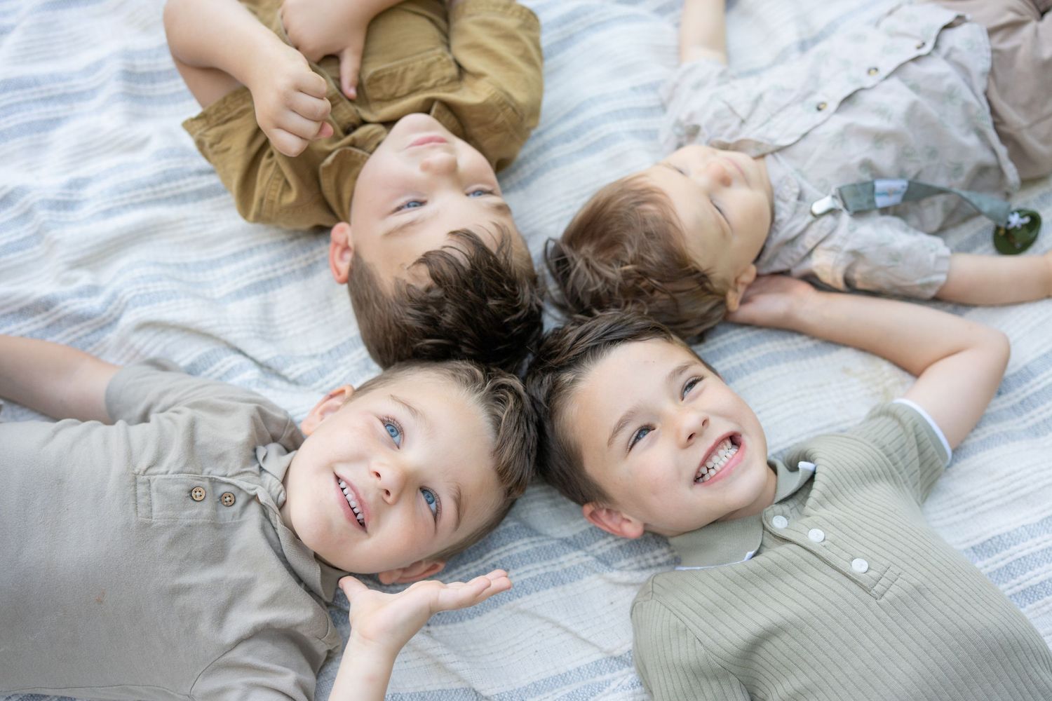 Four happy children lying on a blanket with heads together, smiling and laughing in a joyful group portrait.