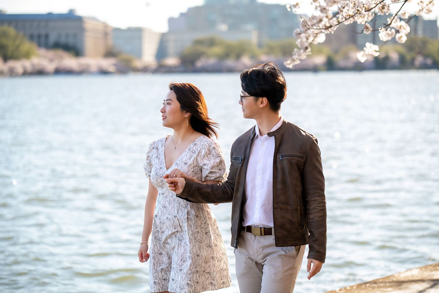 Romantic couple walking along waterfront with cherry blossoms in bloom.