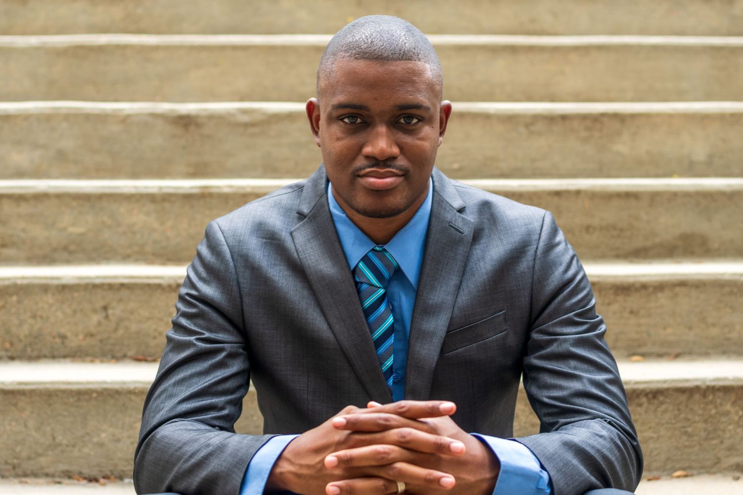 Professional portrait of a businessman in a gray suit and blue tie sitting on steps.