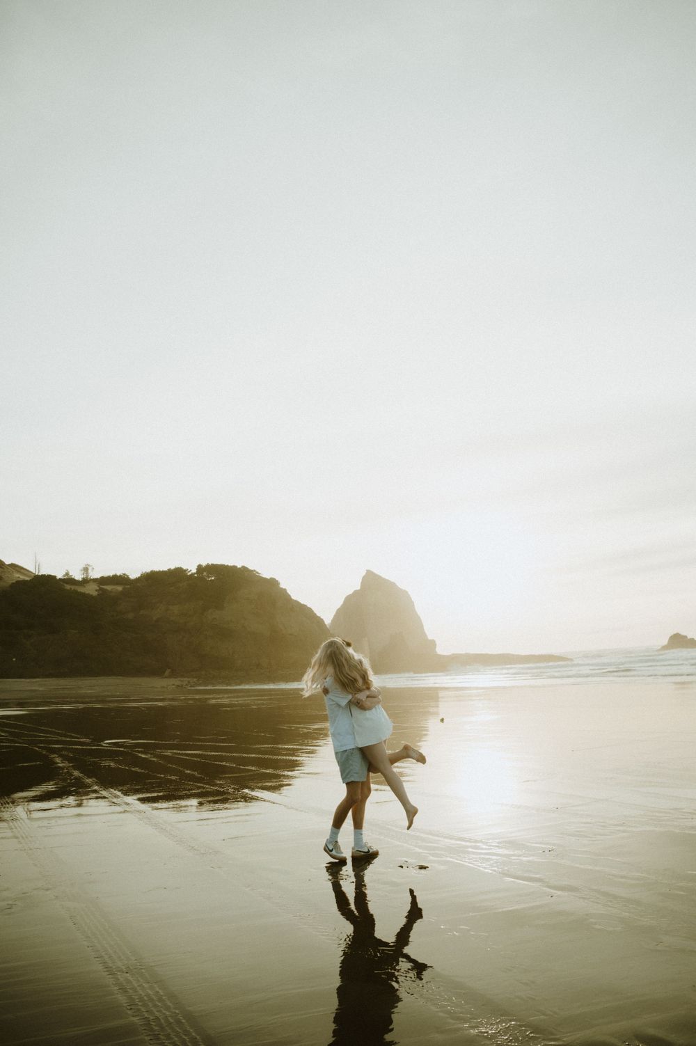 Romantic beach scene with couple dancing in golden sunlight against coastal cliffs.