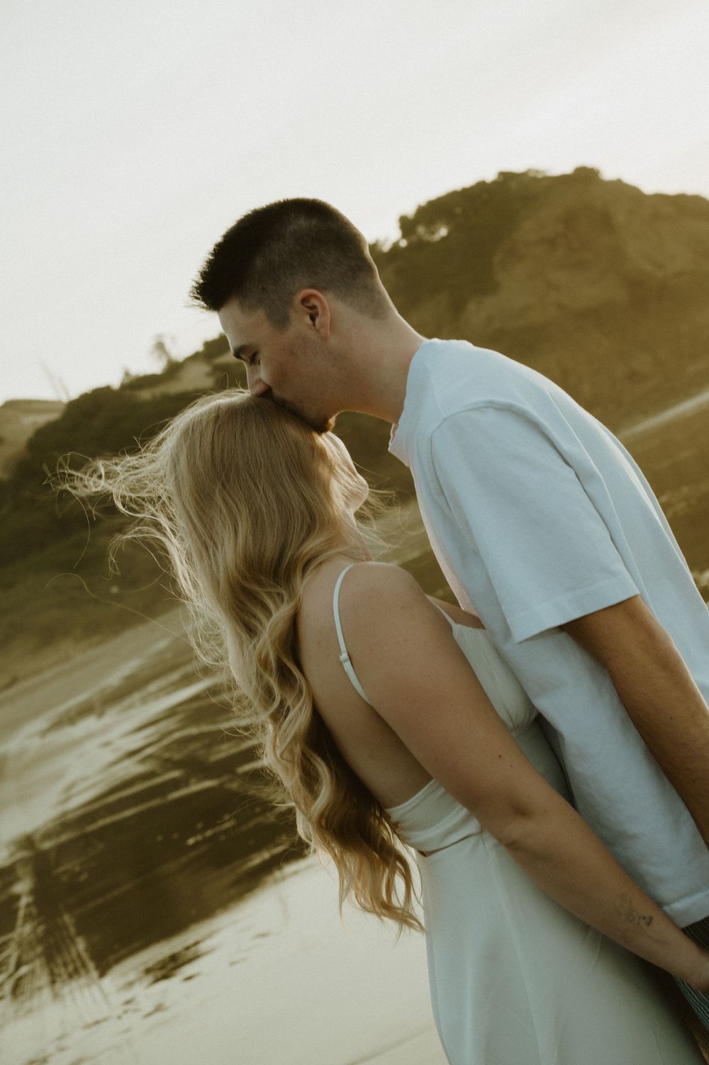 Intimate beach photoshoot captures couple in white clothing during golden hour.