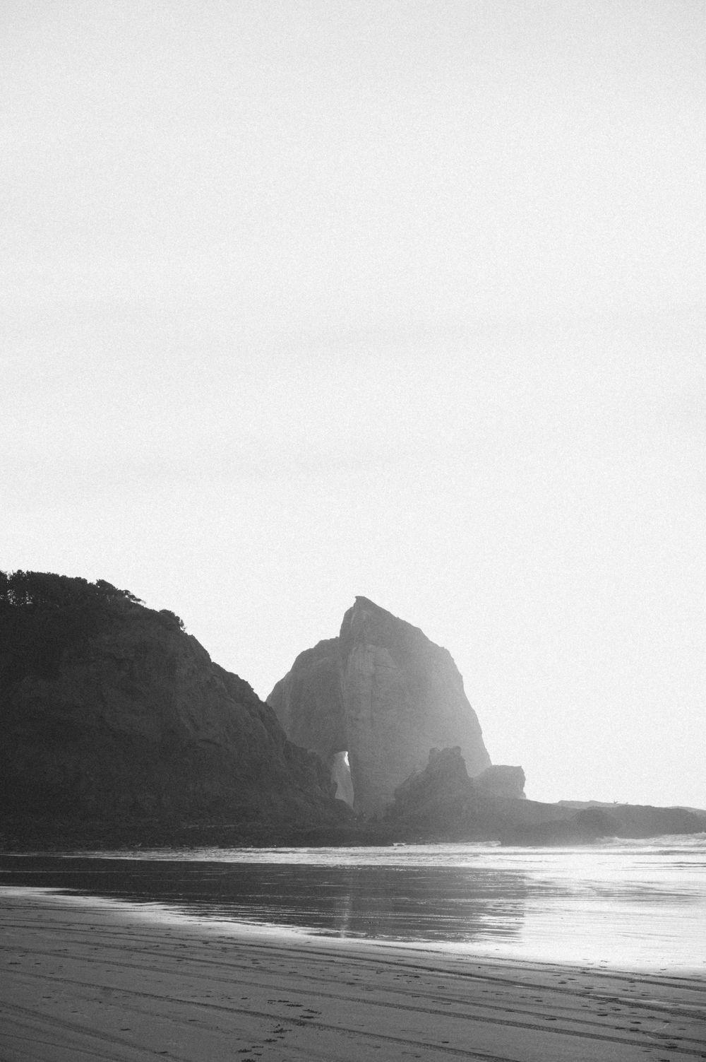 Dramatic black and white coastal landscape with rocky cliffs and ocean waves at sunset.