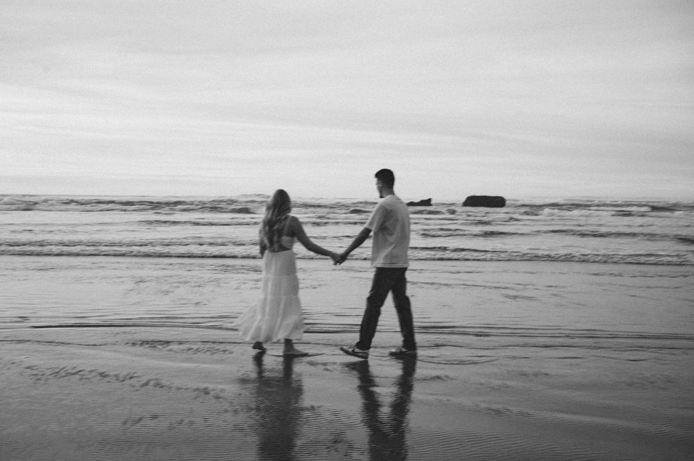 Silhouettes walking along peaceful beach shoreline at dusk.