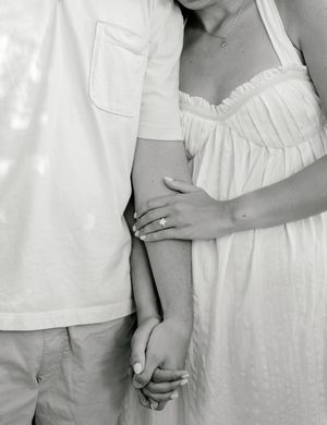 Black and white photo of a couple holding hands, woman wearing white dress and engagement ring.