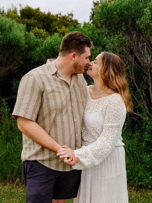 Couple in casual attire sharing a romantic moment against green foliage.