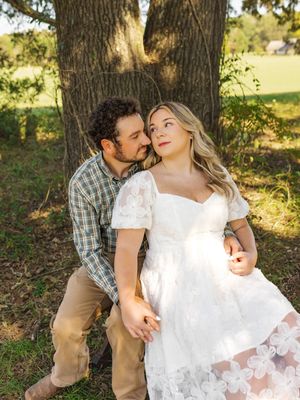 Romantic couple poses by tree trunk in sunlit outdoor setting.