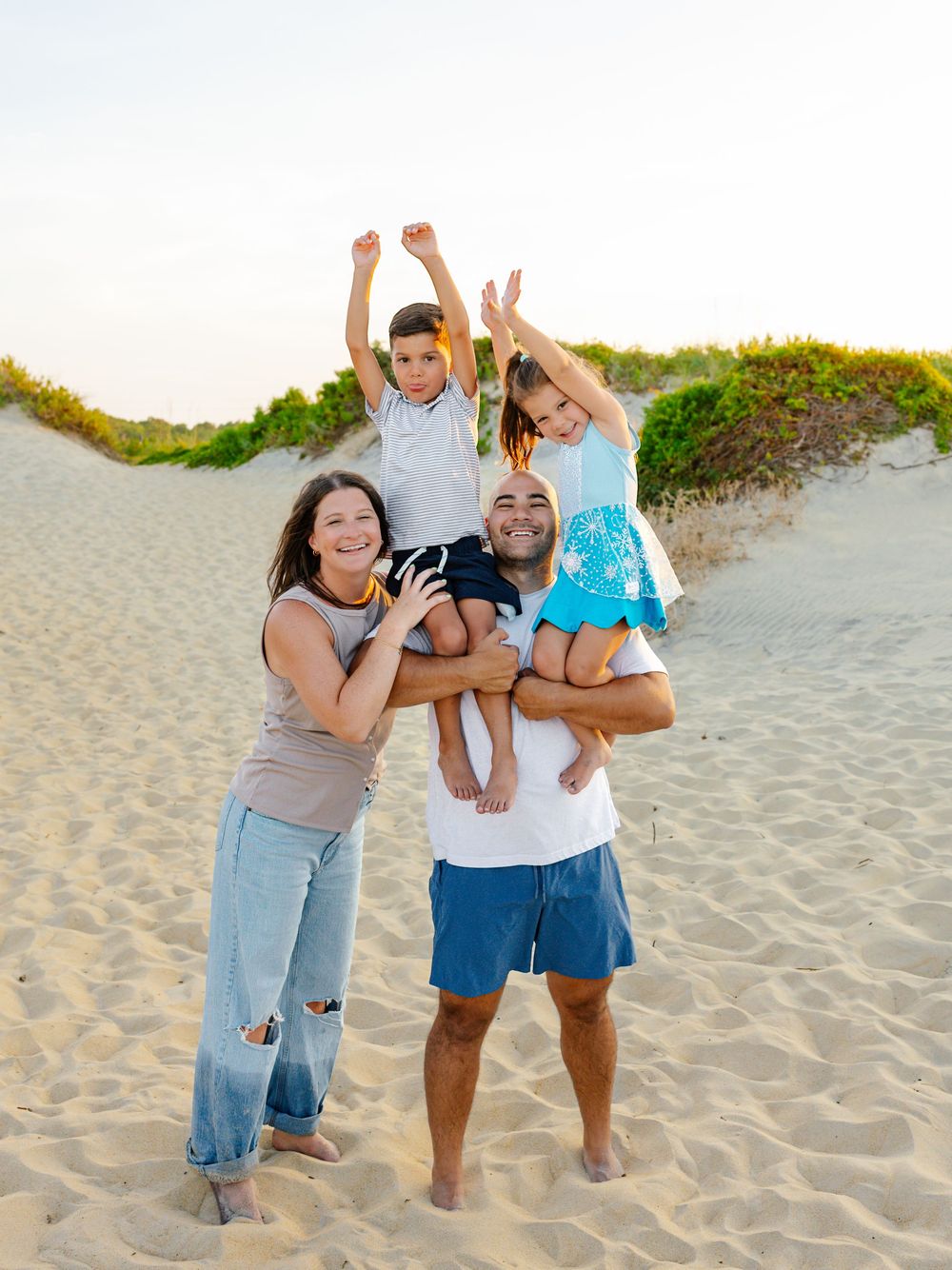 Happy family playing and lifting children at the beach during sunset.