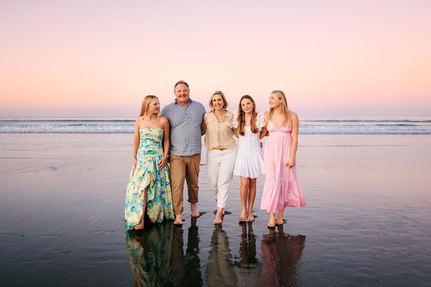 Family of 5 on the beach in Christchurch, Canterbury.  The girls wear pretty dresses and the sunset is pink which is reflected in the water.
