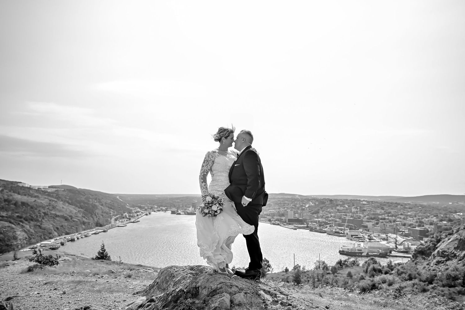 Black-and-white photo of a wedding couple kissing on a windy Signal Hill cliff in 80 km/h gusts.