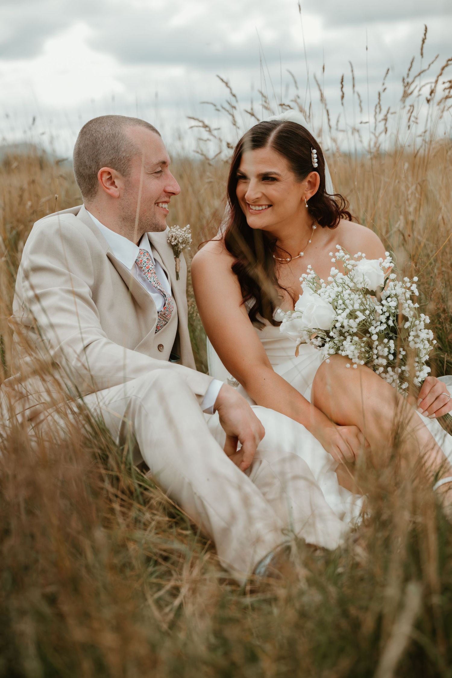 A romantic wedding couple shares intimate moments in a field of tall grass during sunset.