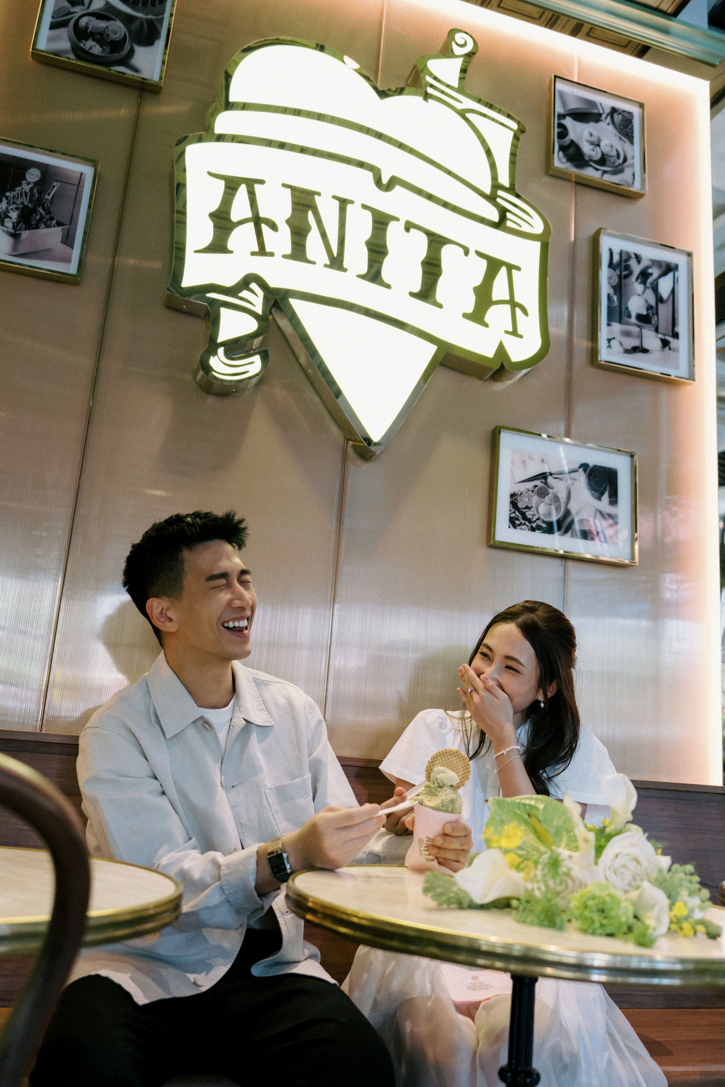 Two people share a joyful moment while dining at a casual restaurant with framed photos on the wall.