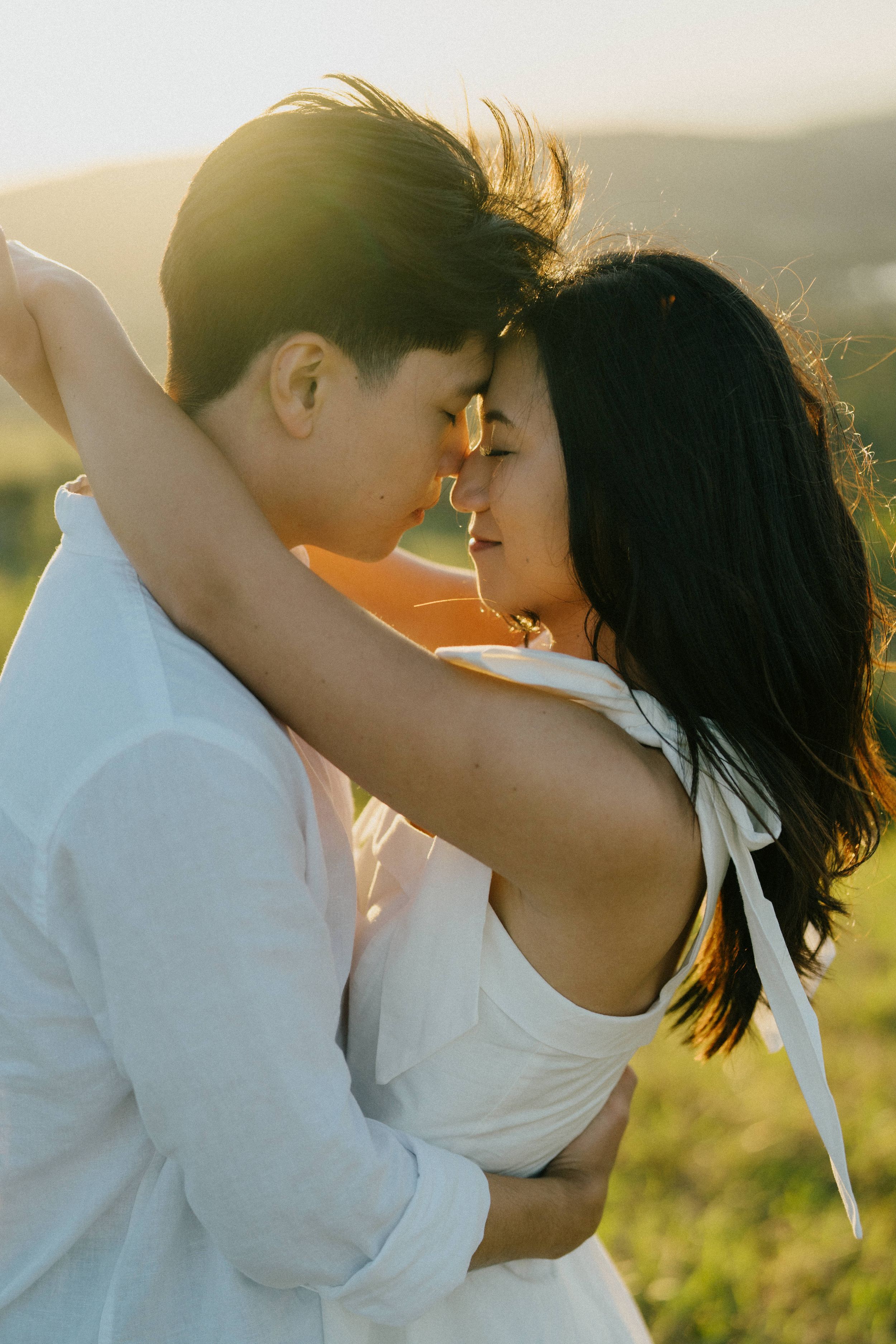 Romantic couple in white outfits embrace while sharing an intimate moment during golden hour sunset.