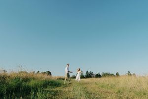 A couple stands together on a grassy hilltop against a clear blue summer sky.