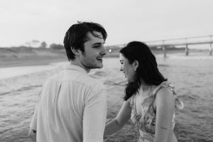 A couple shares a loving moment together on a beach with a bridge visible in the background.