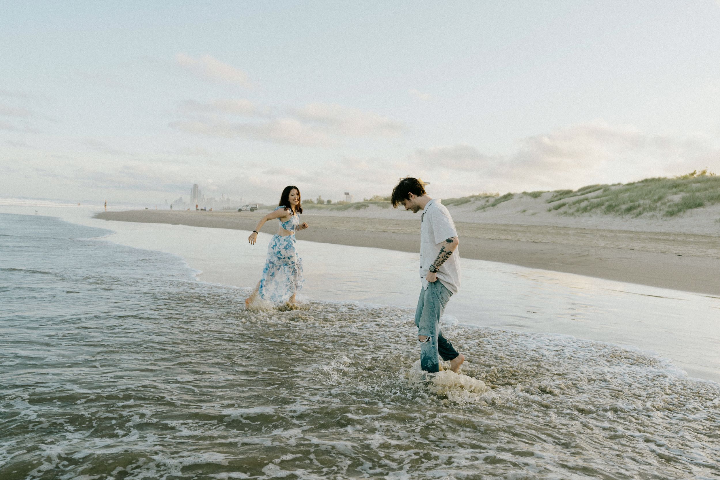 People embrace and walk along a misty beach shoreline at sunset, creating silhouettes against the ocean waves.