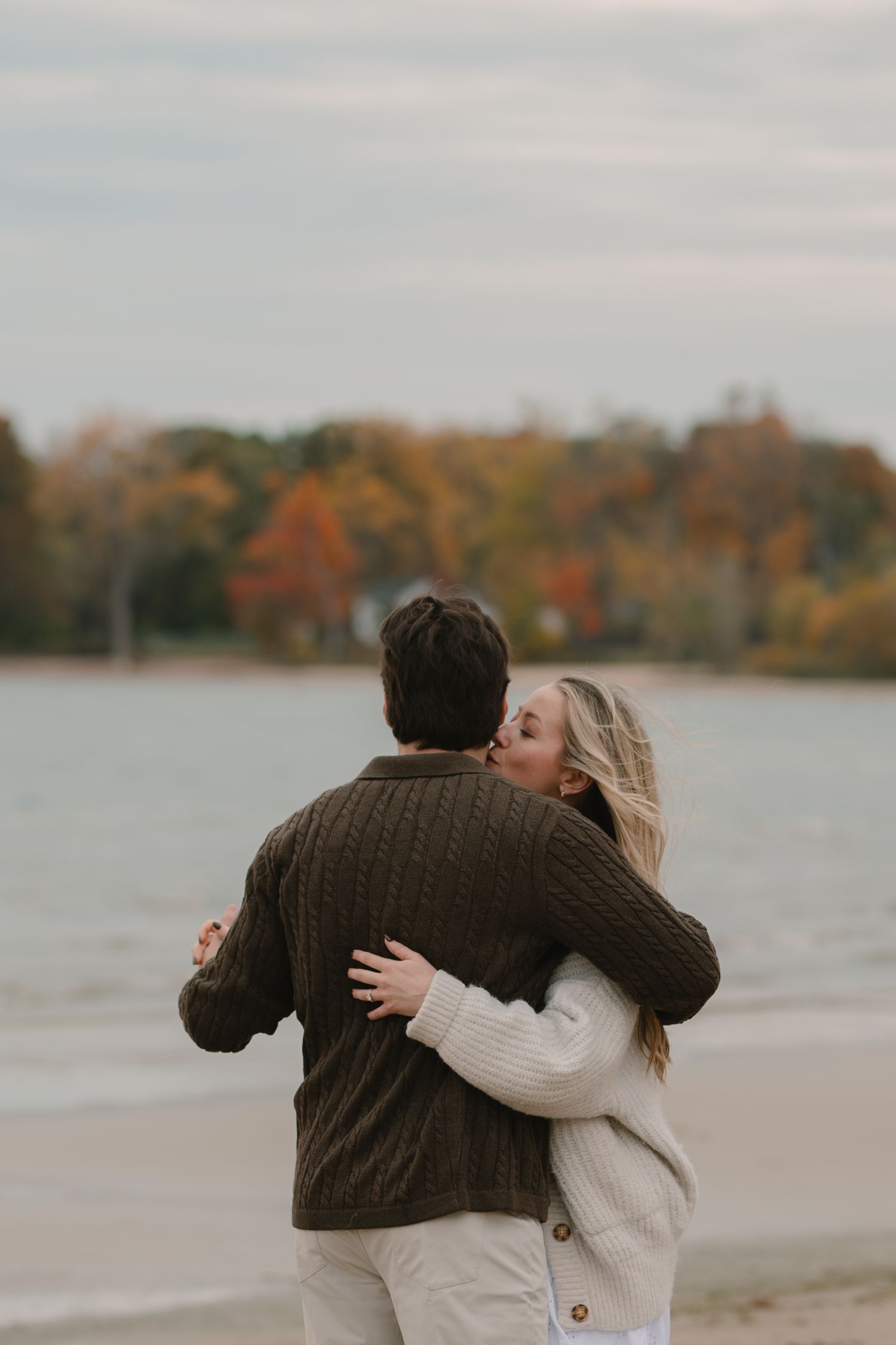 A sequence of romantic moments captured at sunset by a lake with fall foliage in the background.