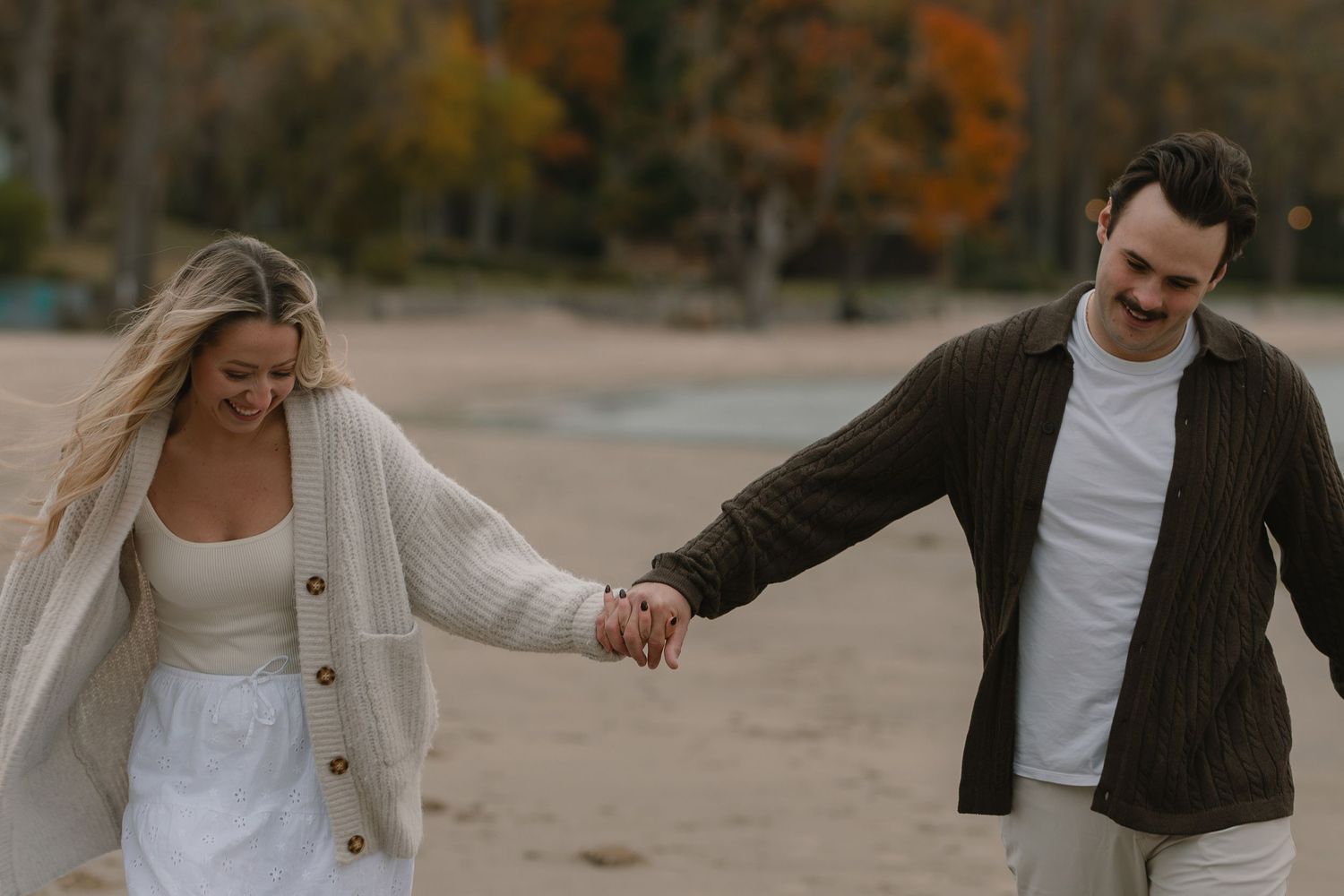 A couple holds hands while walking on a sandy beach path during golden hour.