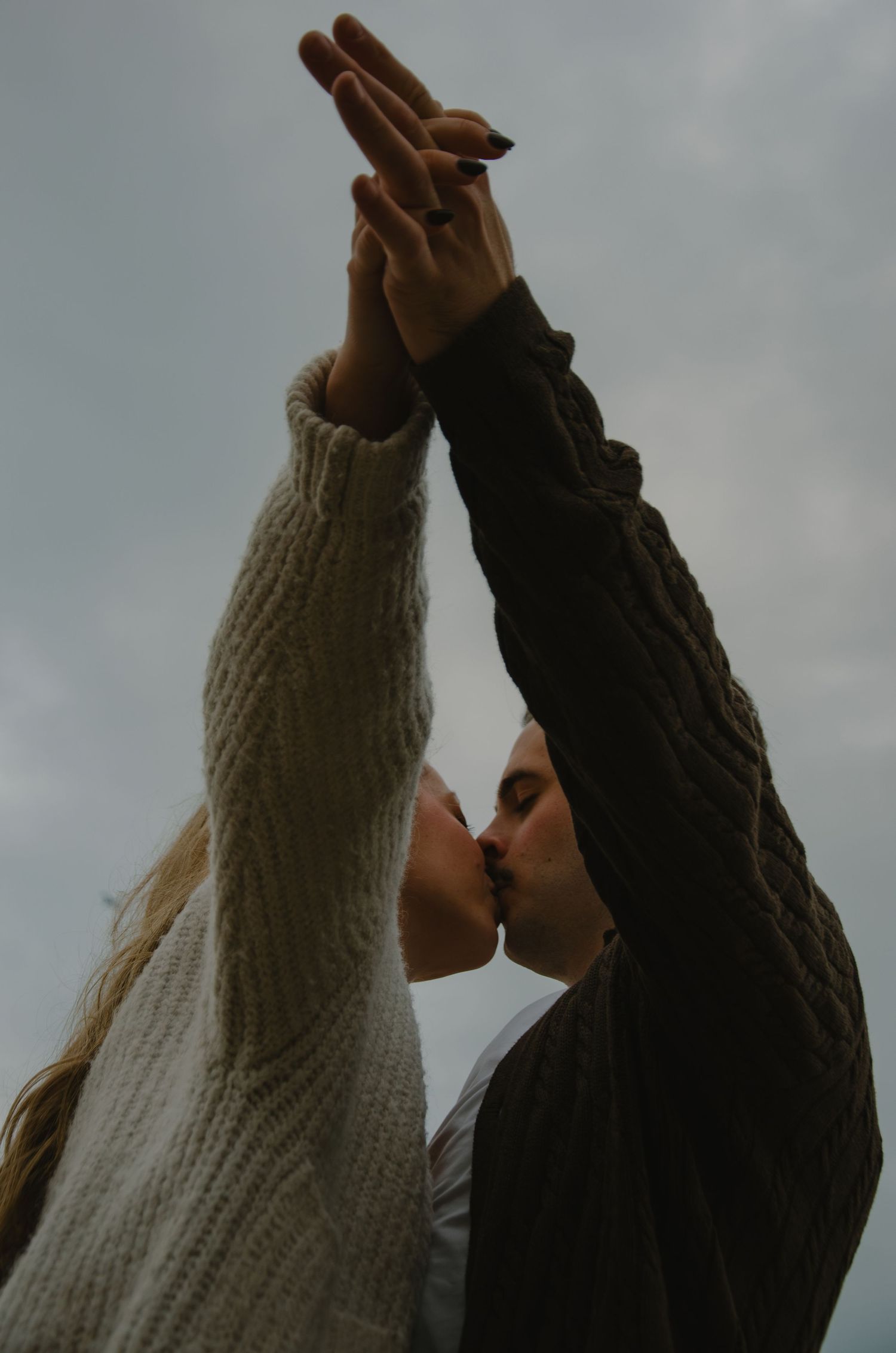 Two people in sweaters raise their hands against a moody grey sky.
