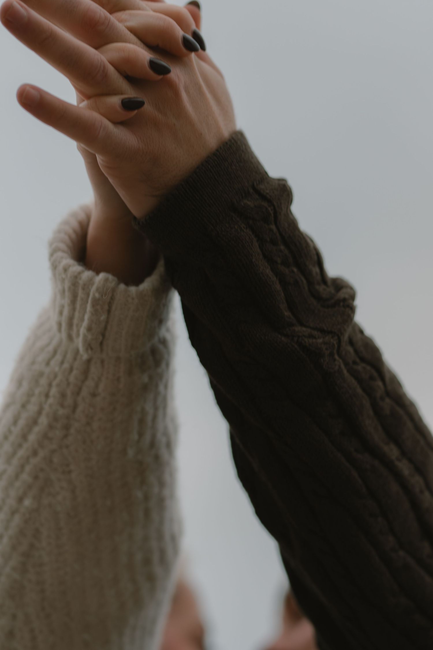 Close-up of hands raised against a grey sky wearing knit sweaters.