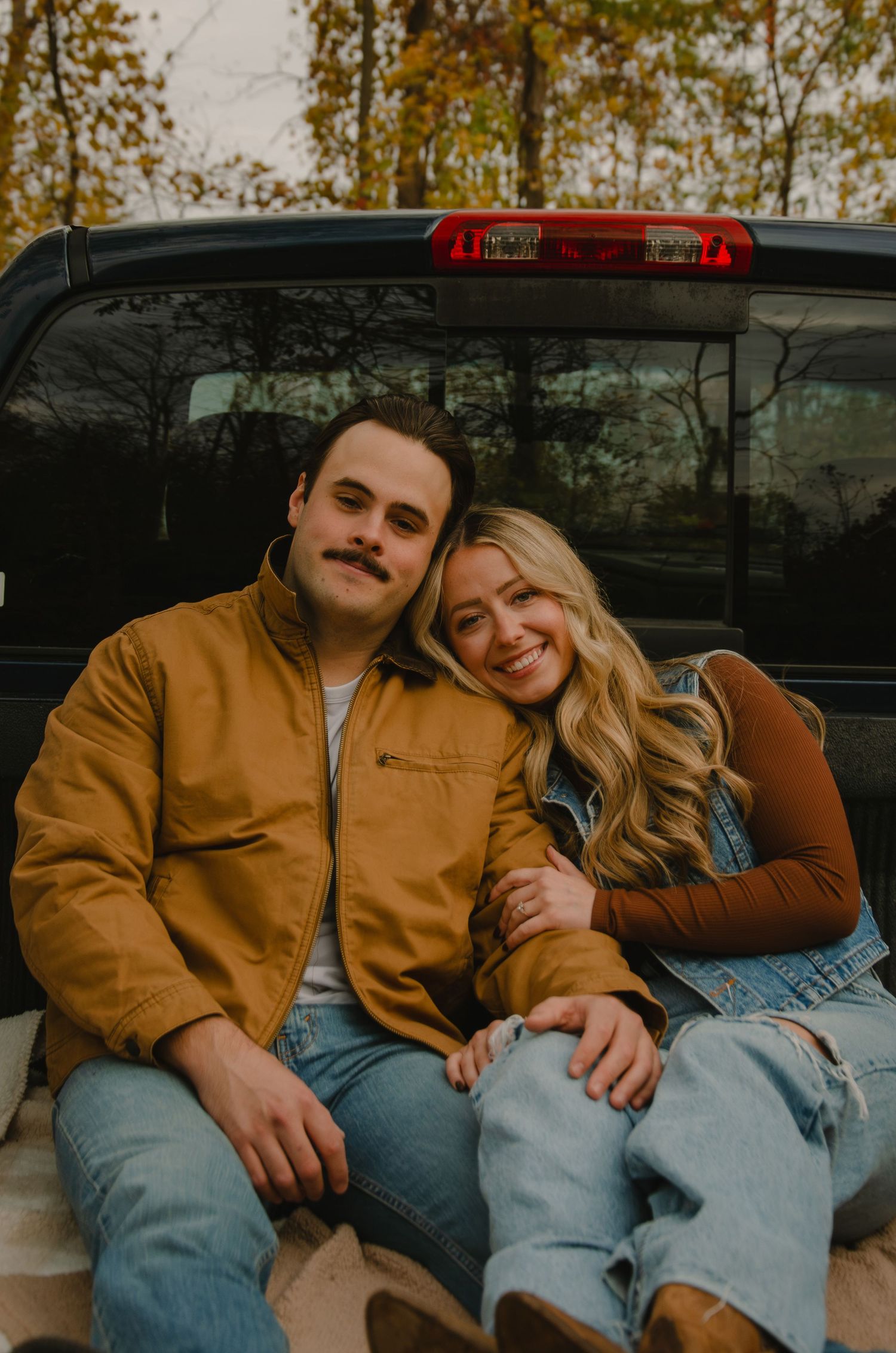 A couple in casual denim and brown jackets sitting together on a bench in autumn.