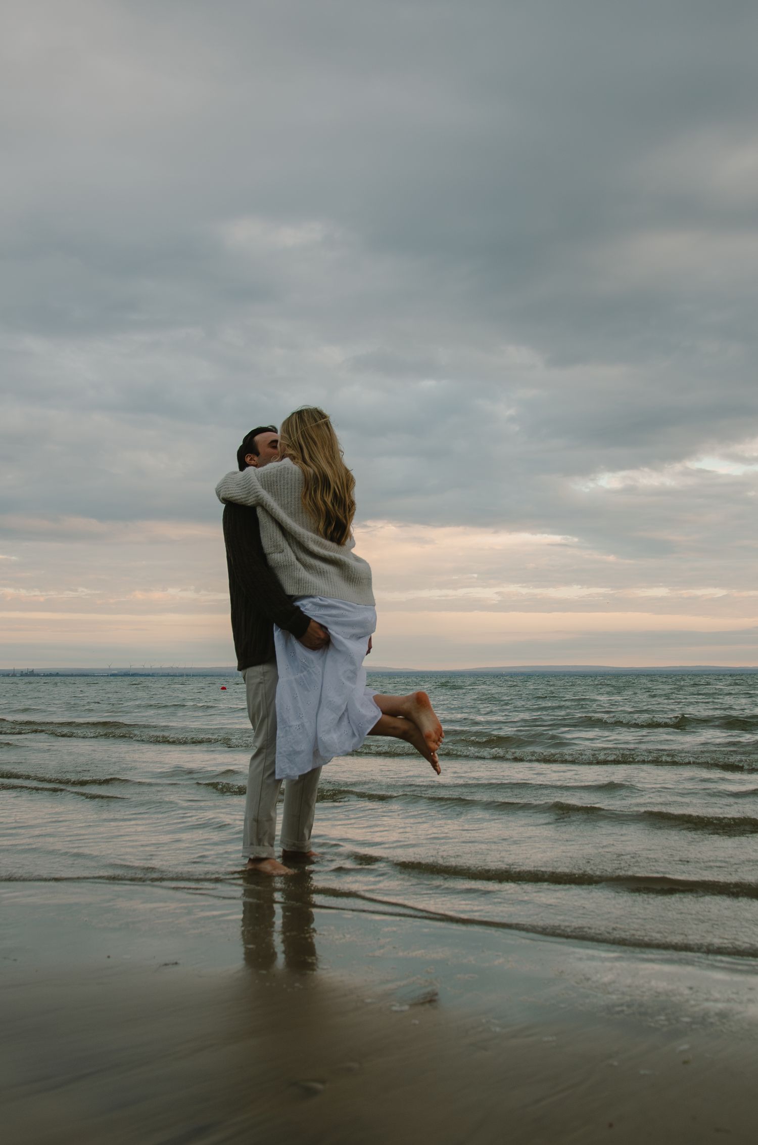 Two people sharing an intimate moment while standing in the ocean waves at dusk.
