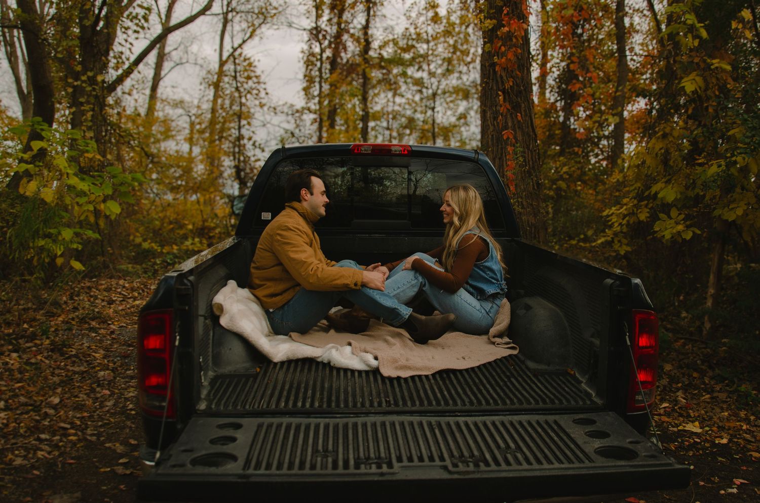 A couple lies in the back of a pickup truck surrounded by autumn trees during a romantic outdoor moment.