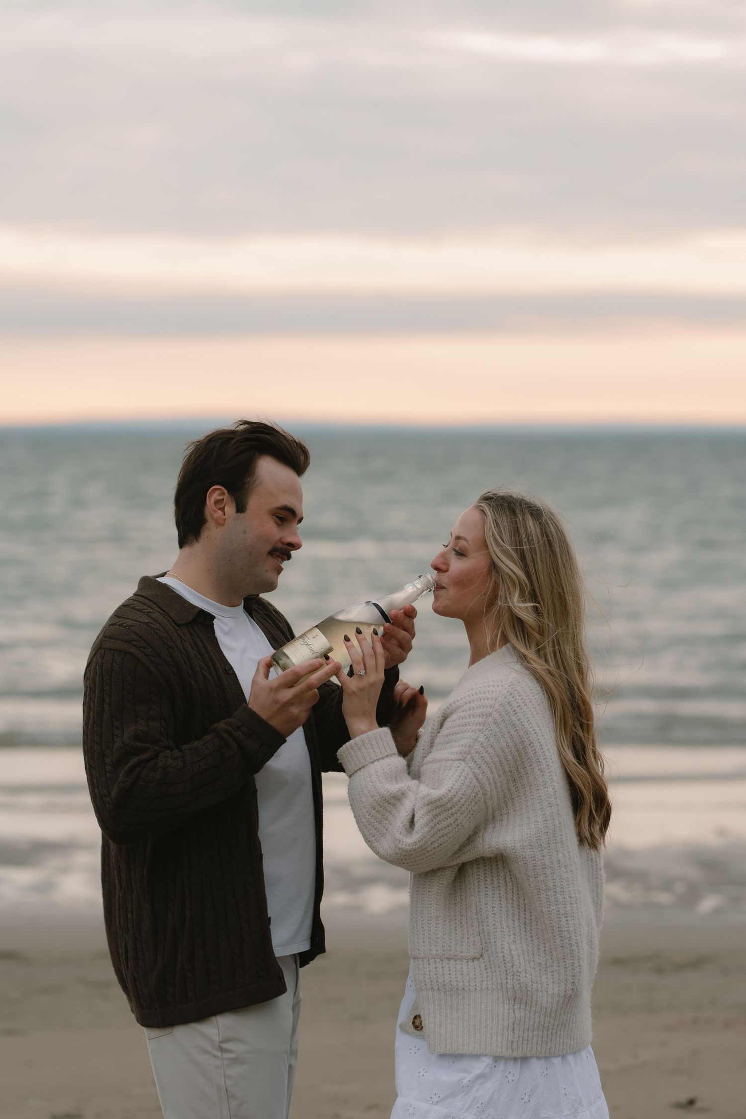 Joyful couple playfully shares ice cream cones together on the beach during their engagement photoshoot.