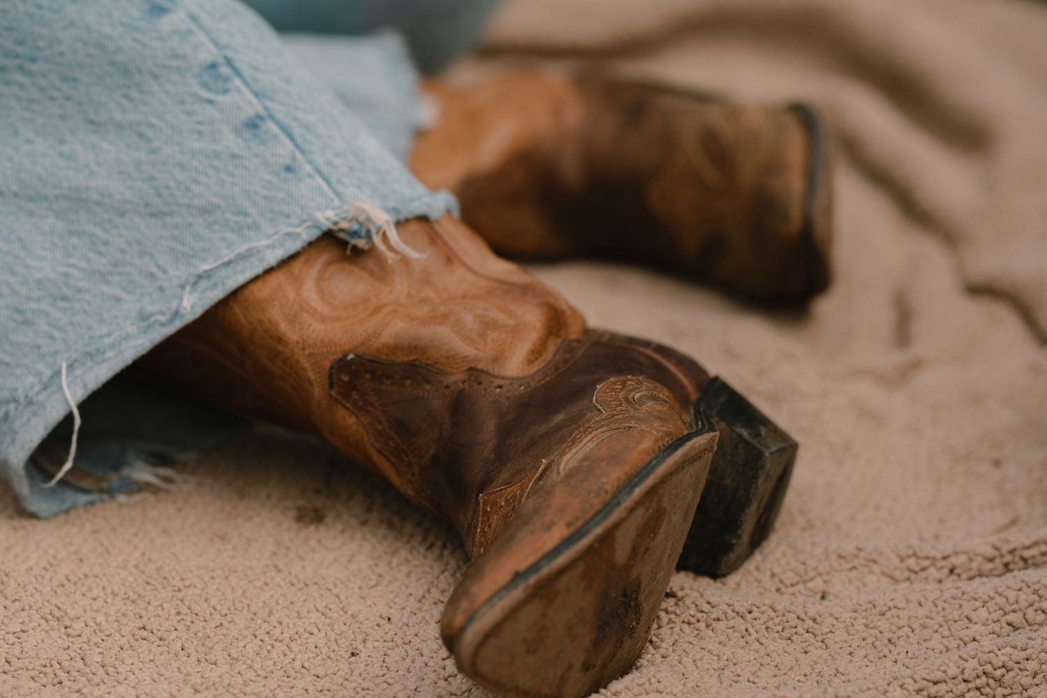 Brown leather boots rest on a textured beige blanket in the back of a truck.