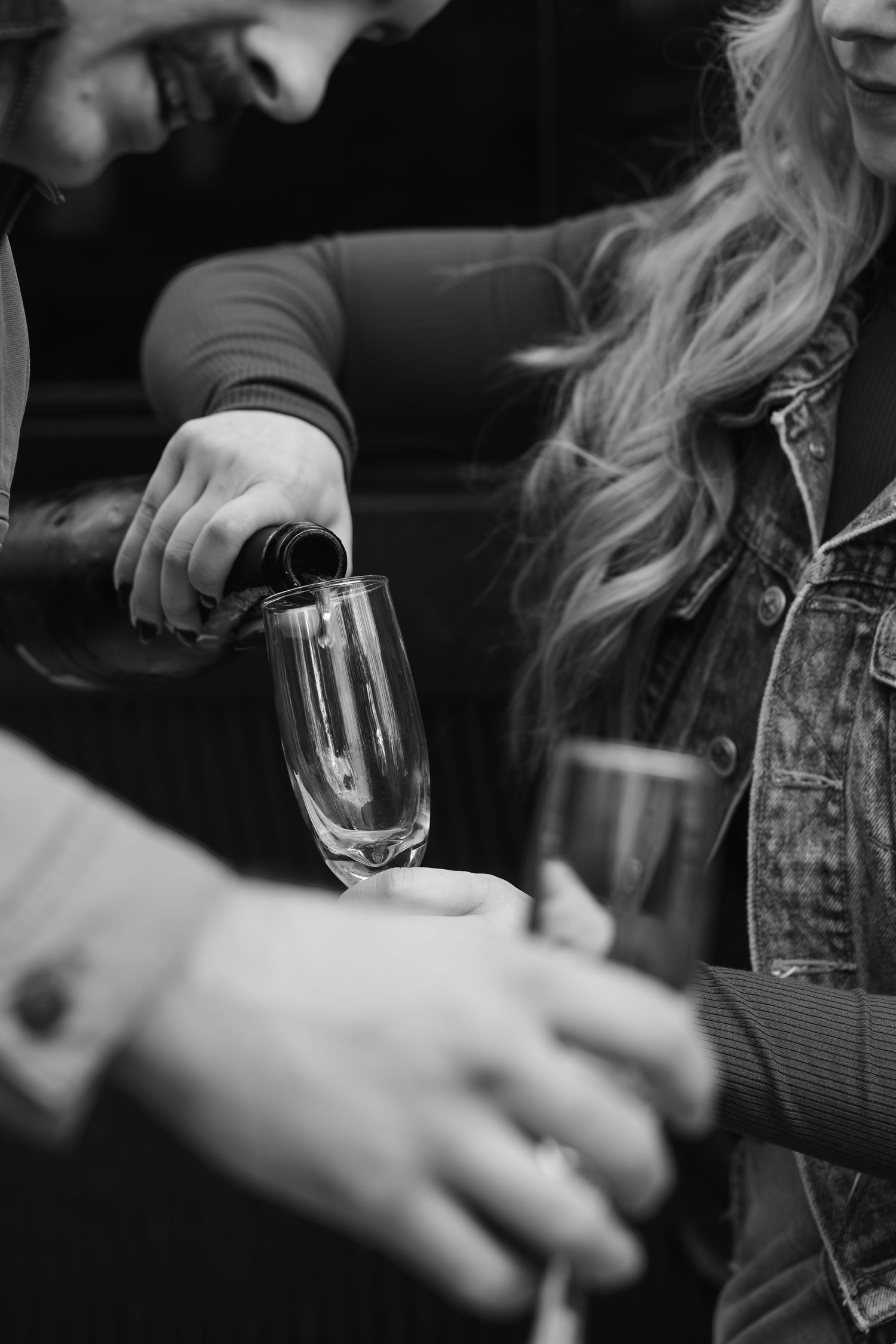 Black and white close-up shot of hands holding wine glasses in a dimly lit setting.